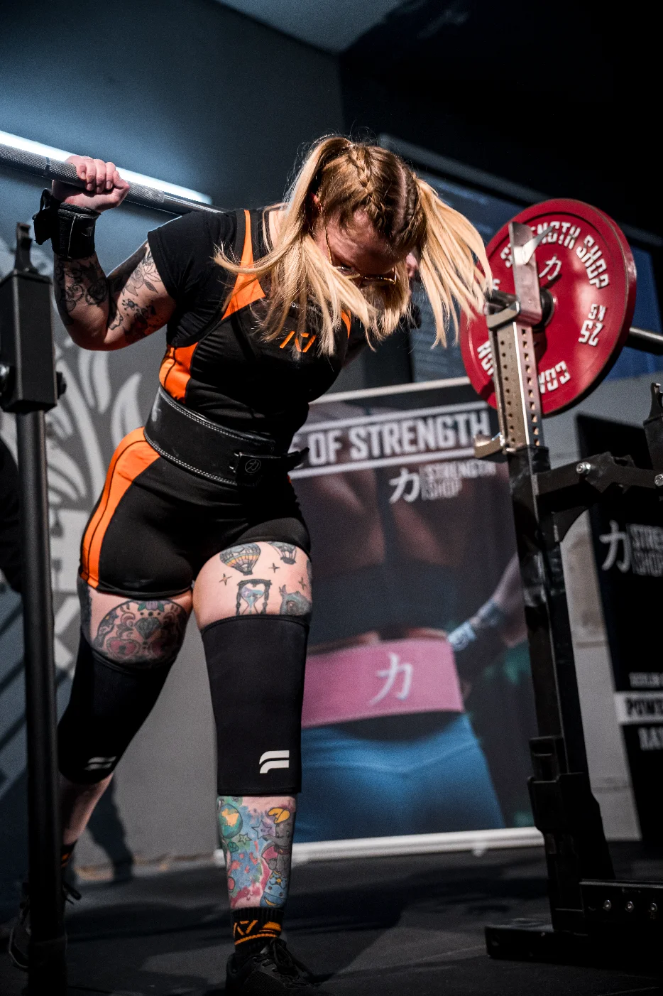 Athletin mit der Hantel im Nacken am Rack, Kopf gesenkt und Haare im Gesicht