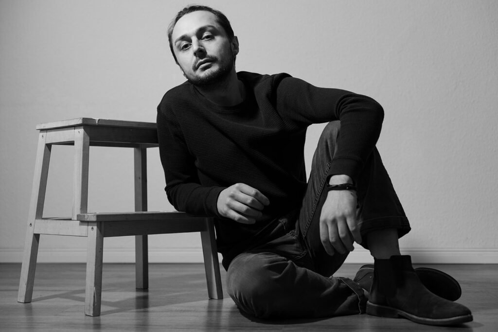 portrait of a man sitting on the floor leaning against a chair
